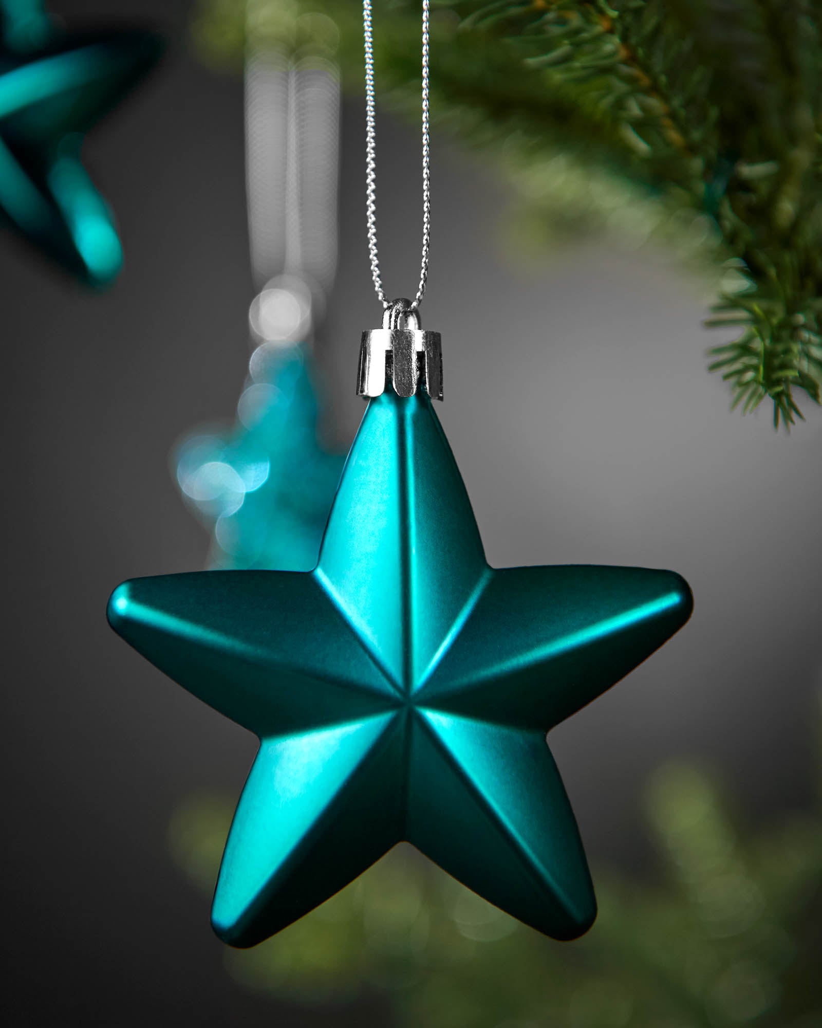 Close-up of a shiny teal 7cm star decoration with a silver hanging string.
