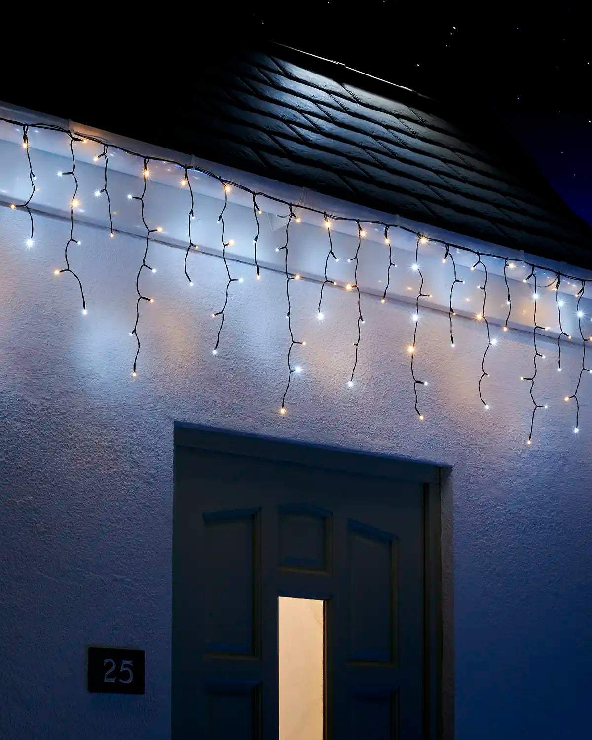 Warm white and white icicle lights hanging above an exterior doorway at night.