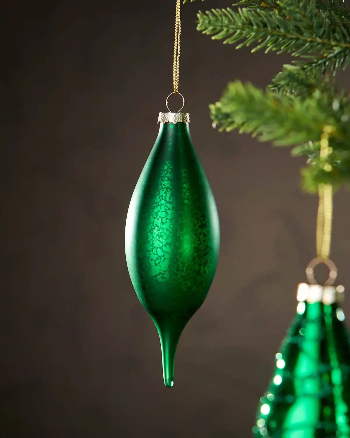 two Green glass baubles hanging on a tree with a dark background