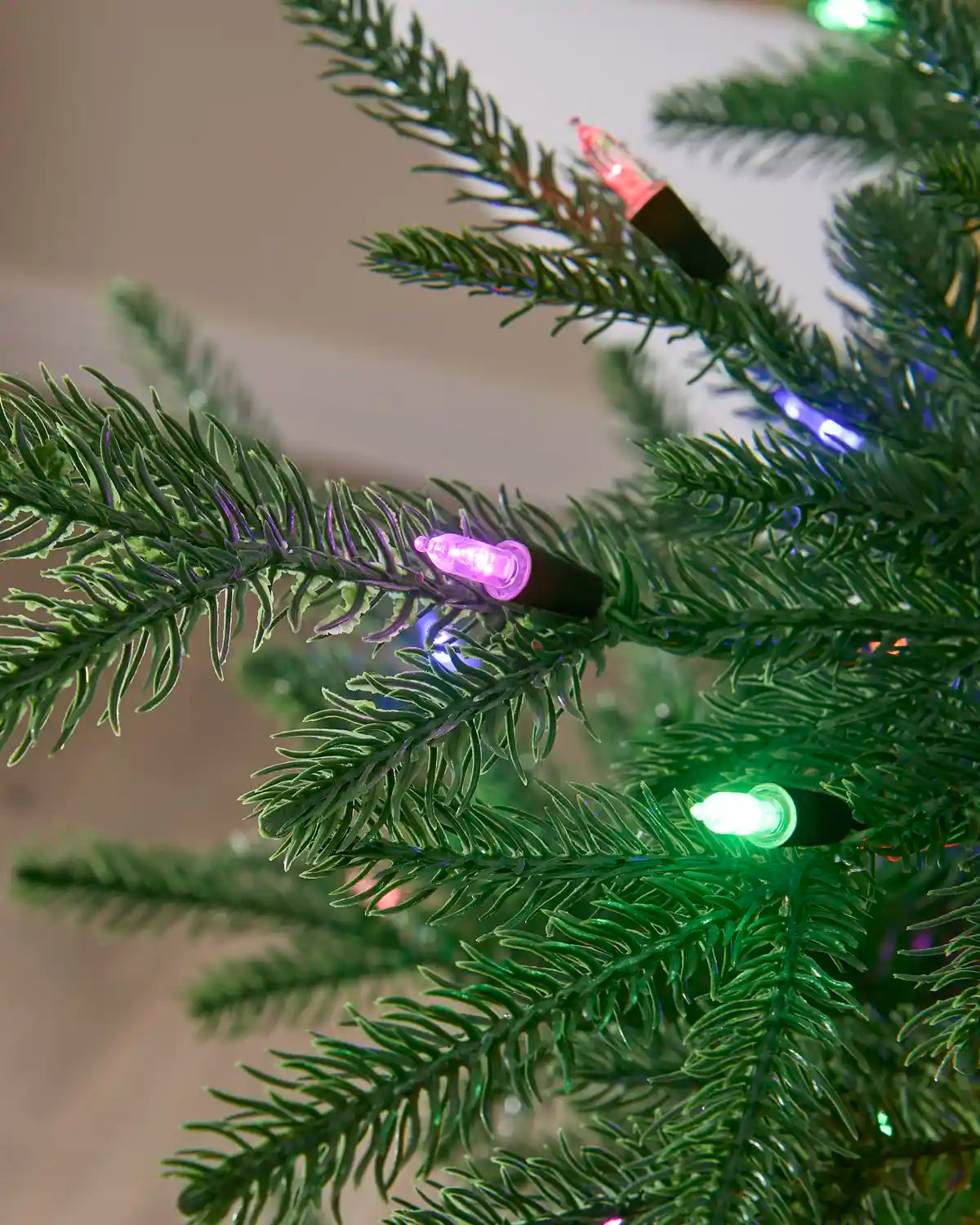 Close-up of multi-colour candle-style LED bulbs illuminated among Christmas tree branches.