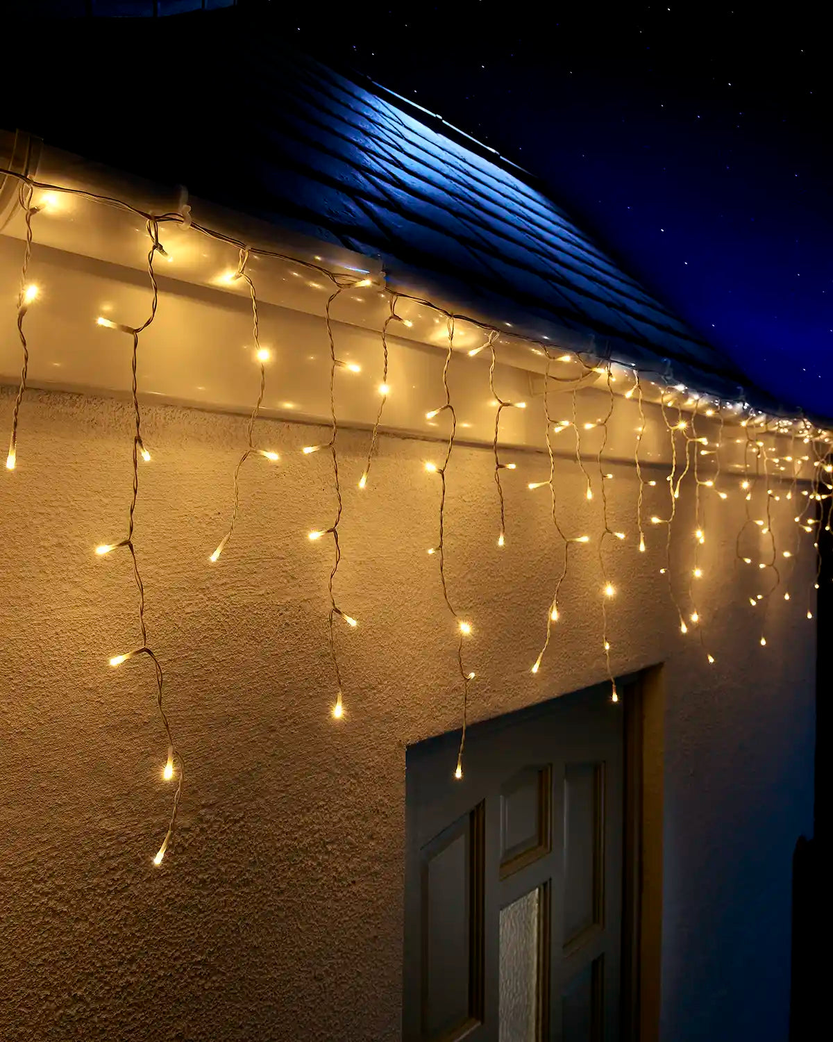 Warm white icicle lights on white cable hanging above an outdoor doorway at night.
