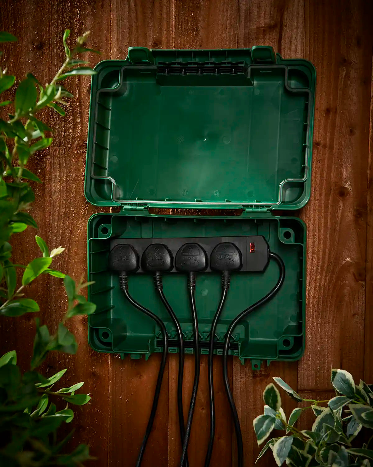 Open green weatherproof electrical box mounted on a fence with plugs connected inside.