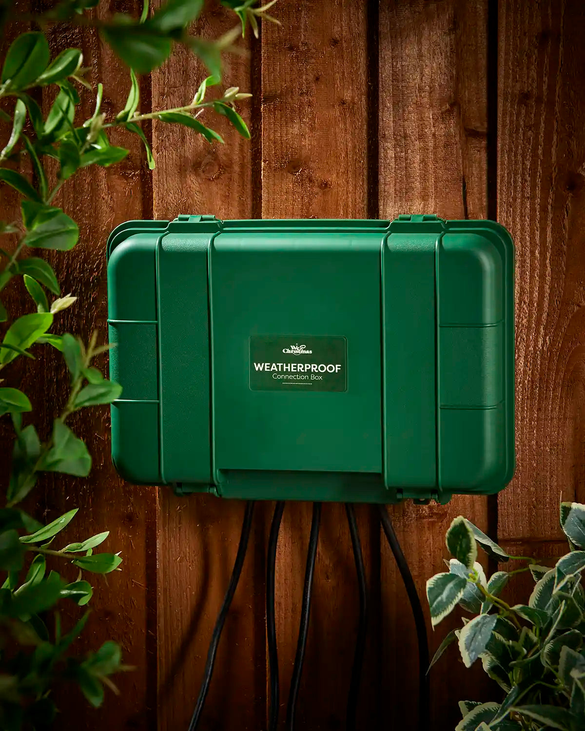 Green weatherproof electrical box mounted on a wooden fence with cables below.