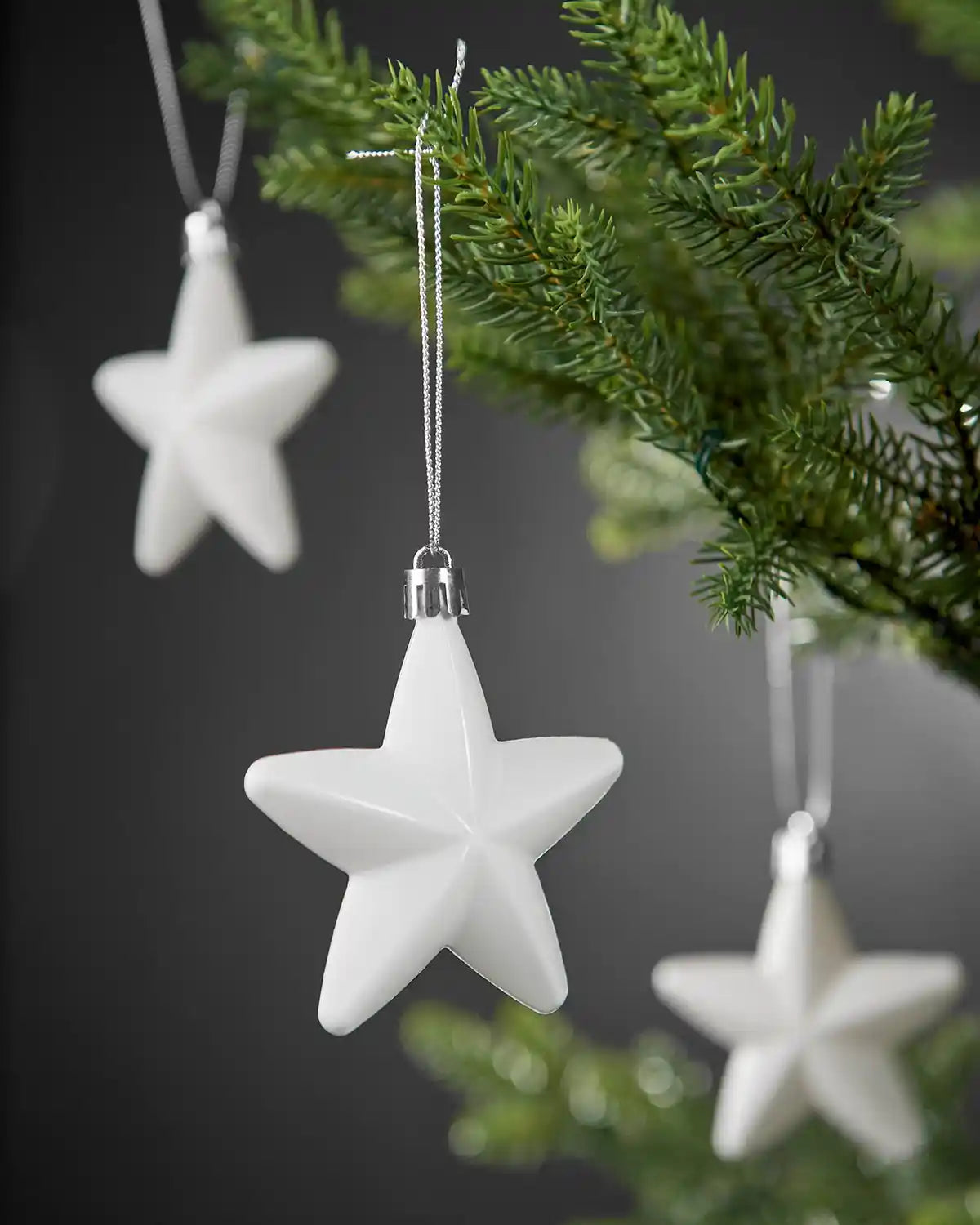 White 7cm star ornament hanging from a Christmas tree branch.