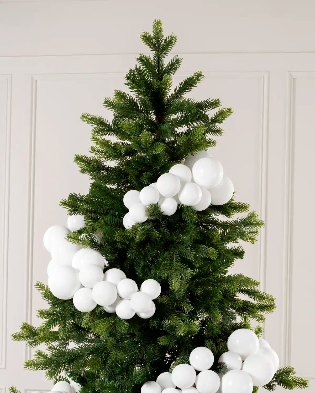 White bauble cluster arch arranged through the upper branches of a green Christmas tree.