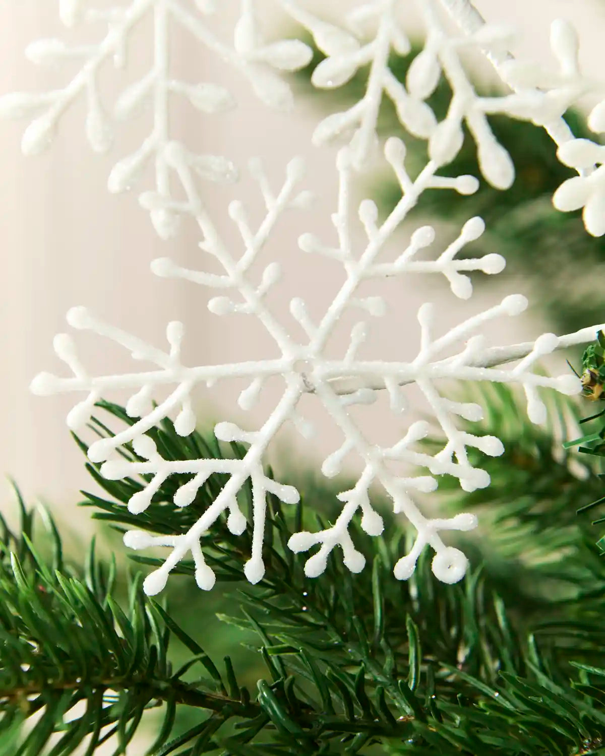Detailed close-up of a white glitter snowflake decoration against green Christmas tree branches.