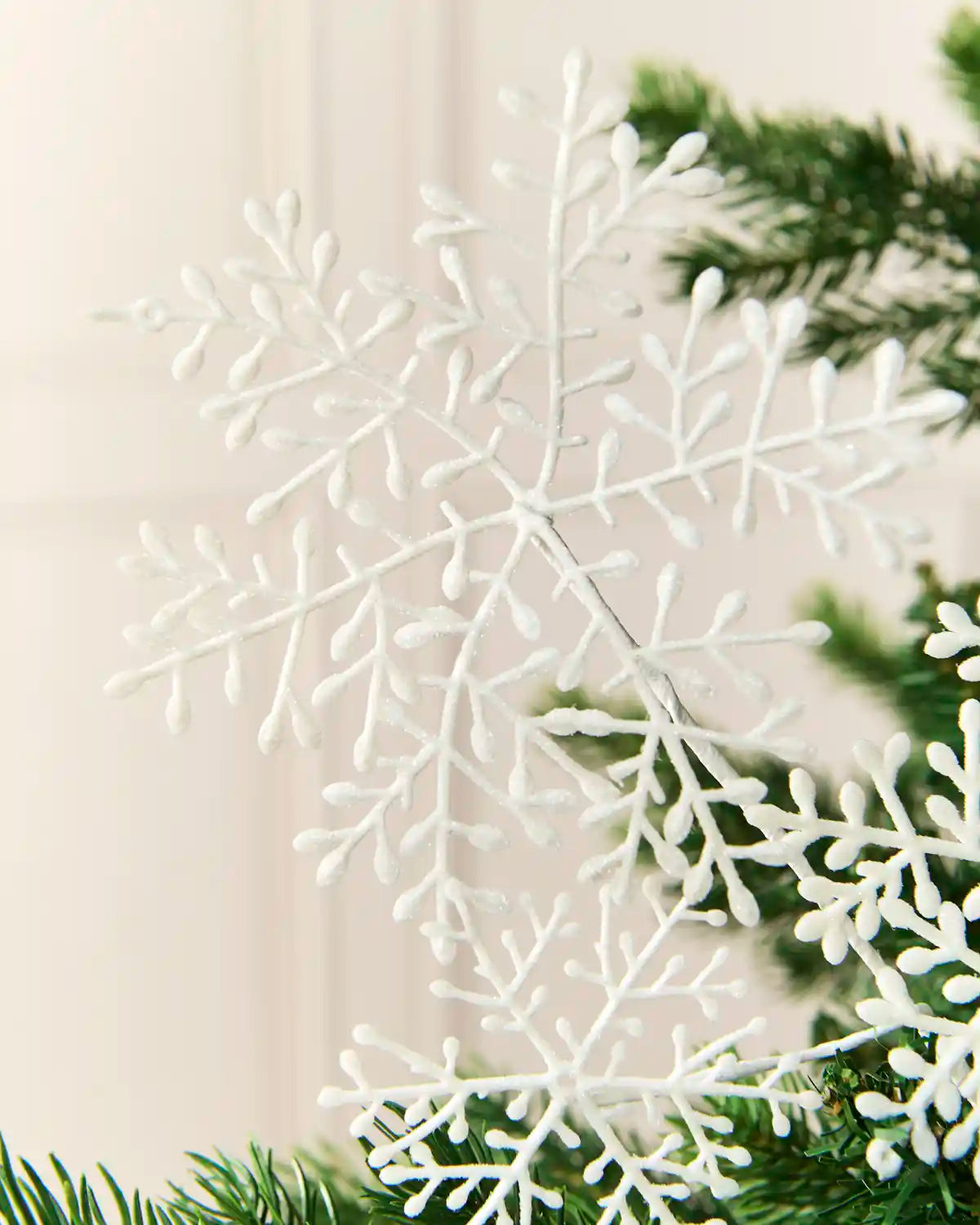 Close-up of a white glitter snowflake spray displayed within Christmas tree foliage.