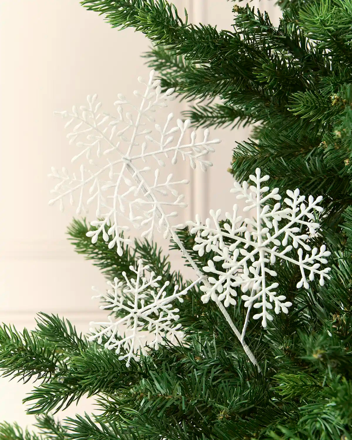 White glitter snowflake sprays arranged among the branches of a green Christmas tree.
