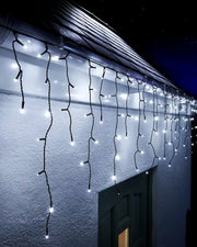 White icicle lights on black cable hanging along a roofline above an exterior wall and doorway at night.