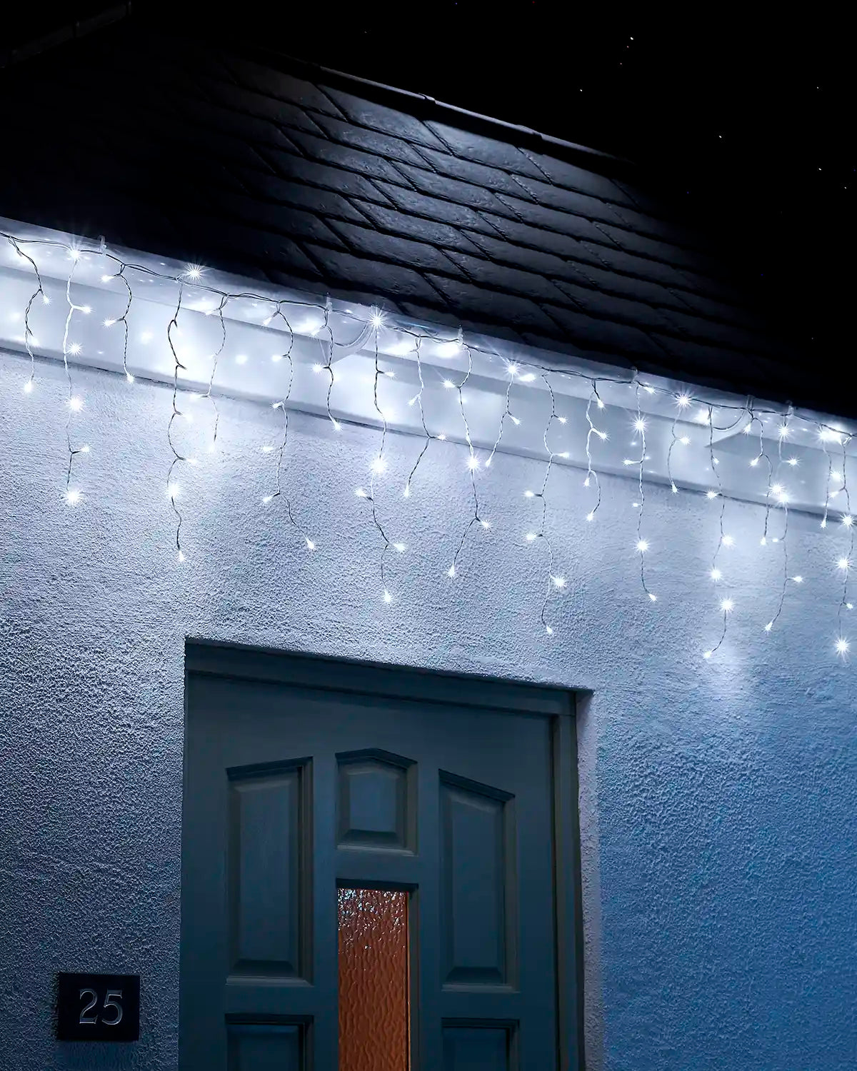 White icicle lights on white cable displayed along a roofline above a front door at night.