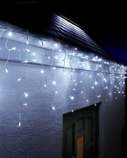 White icicle lights on white cable hanging above an exterior wall and doorway at night.