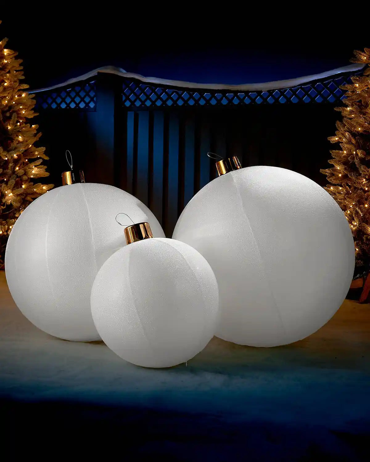 White inflatable tinsel Christmas baubles in different sizes displayed outdoors with warm festive lights.