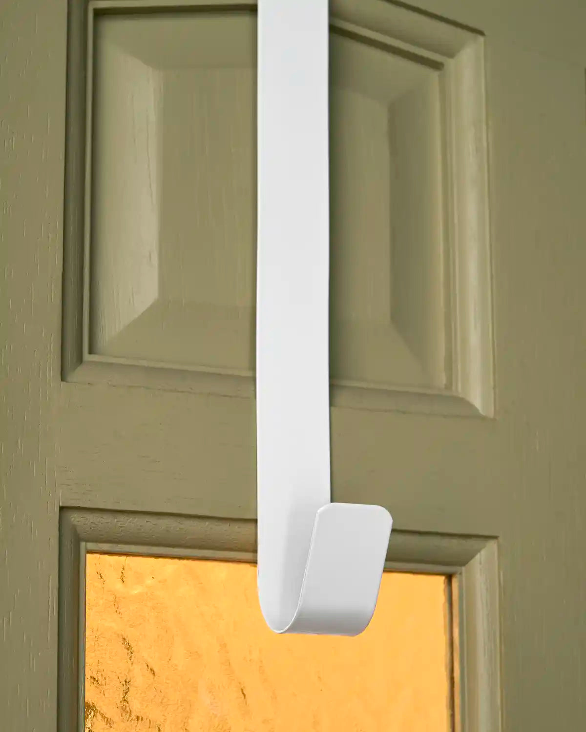 Close-up of the white metal wreath hanger showing the curved lower hook fitted on a door.