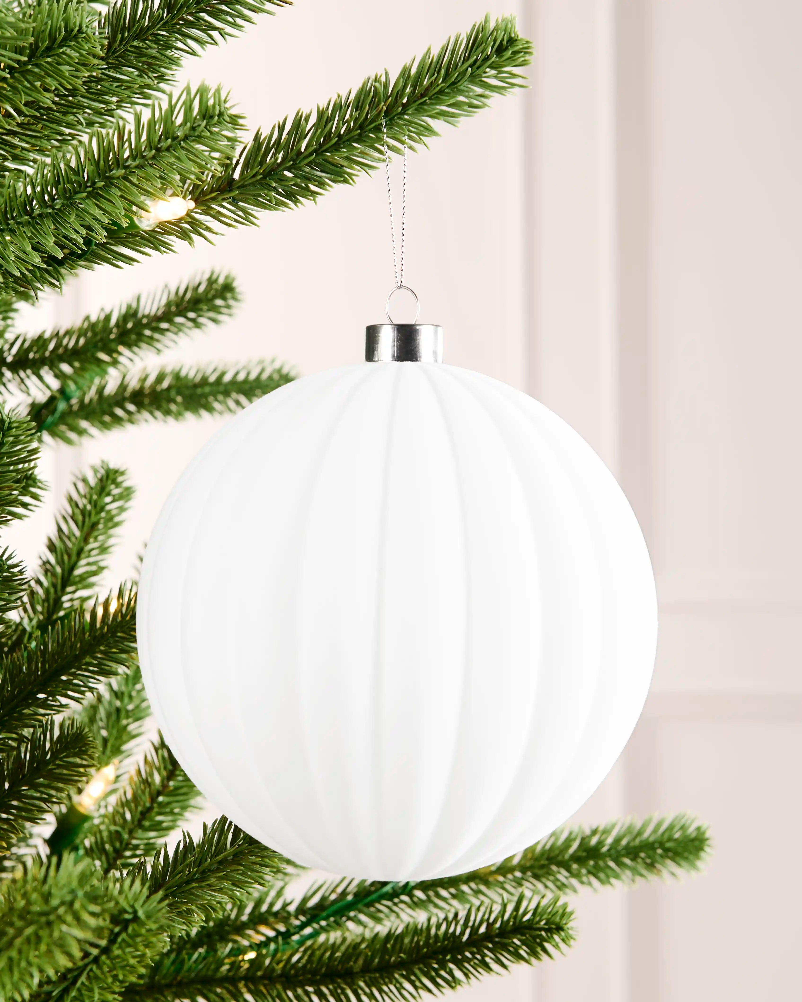 15 cm white oversized velvet ribbed bauble hanging from a Christmas tree with a silver cap.
