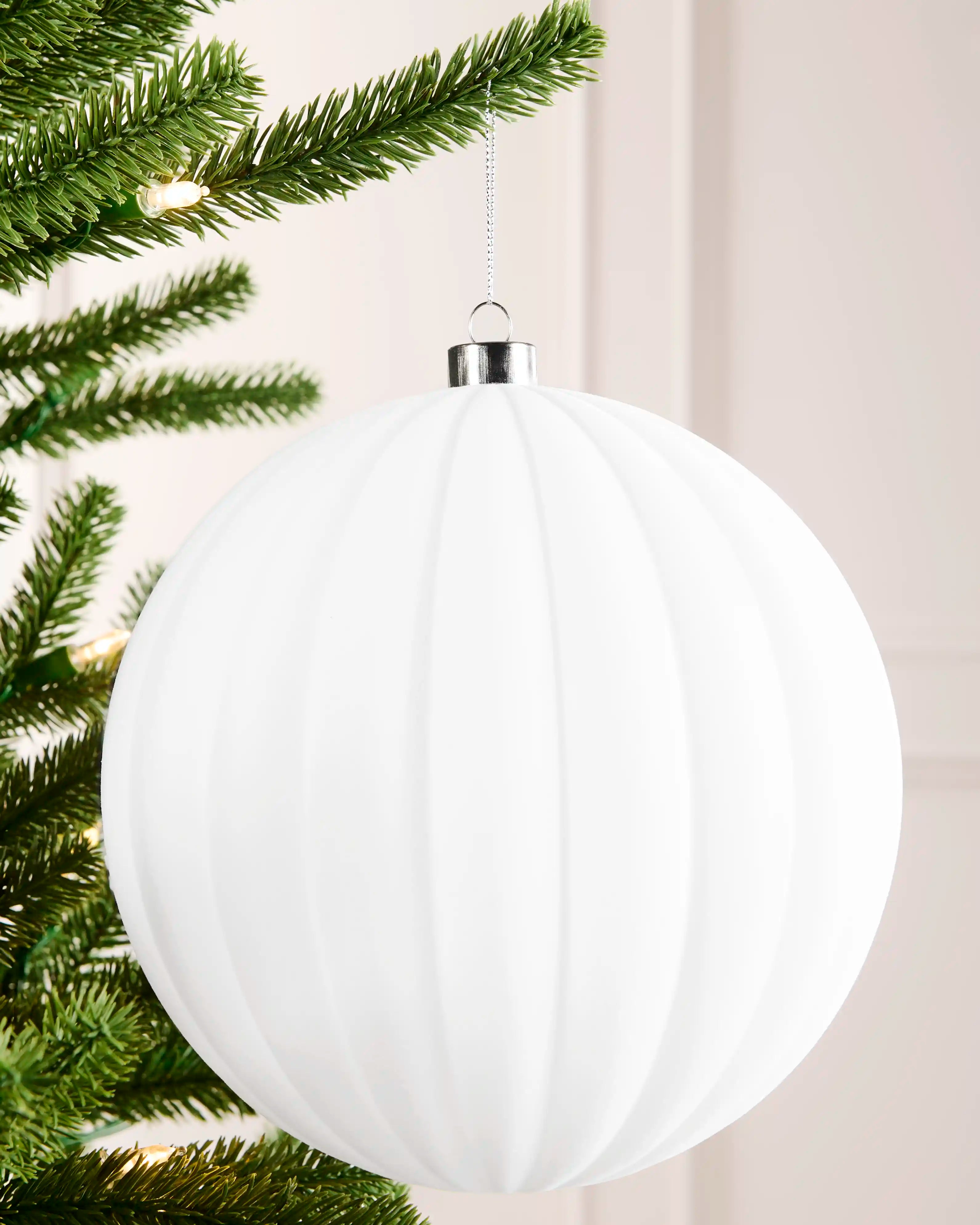 20 cm white oversized velvet ribbed bauble hanging from a Christmas tree with a silver cap and silver hanging string.