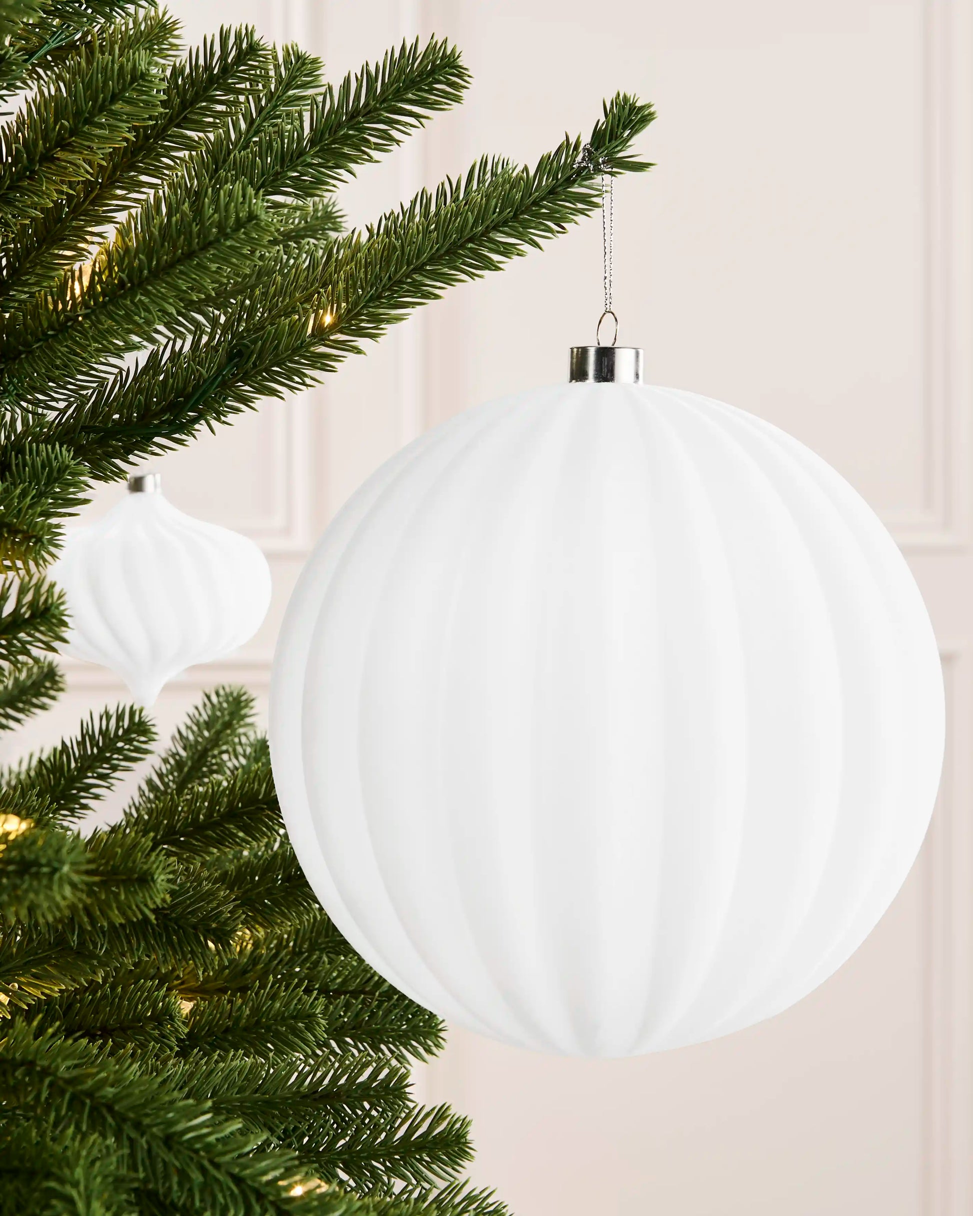 White 20 cm oversized velvet ribbed bauble displayed on a Christmas tree with a matching white ornament in the background.