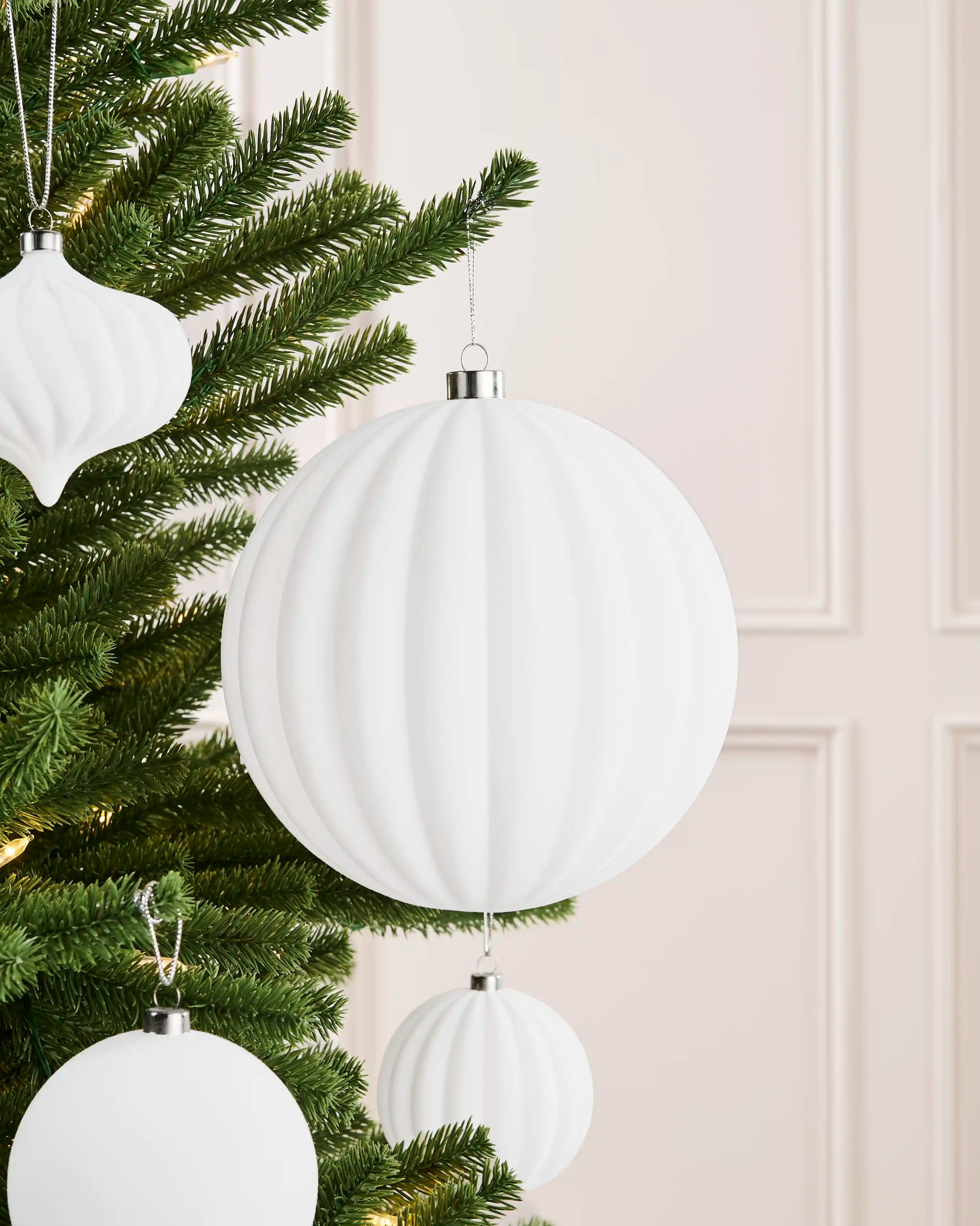 Oversized 20 cm white velvet ribbed bauble styled among matching decorations on a Christmas tree.