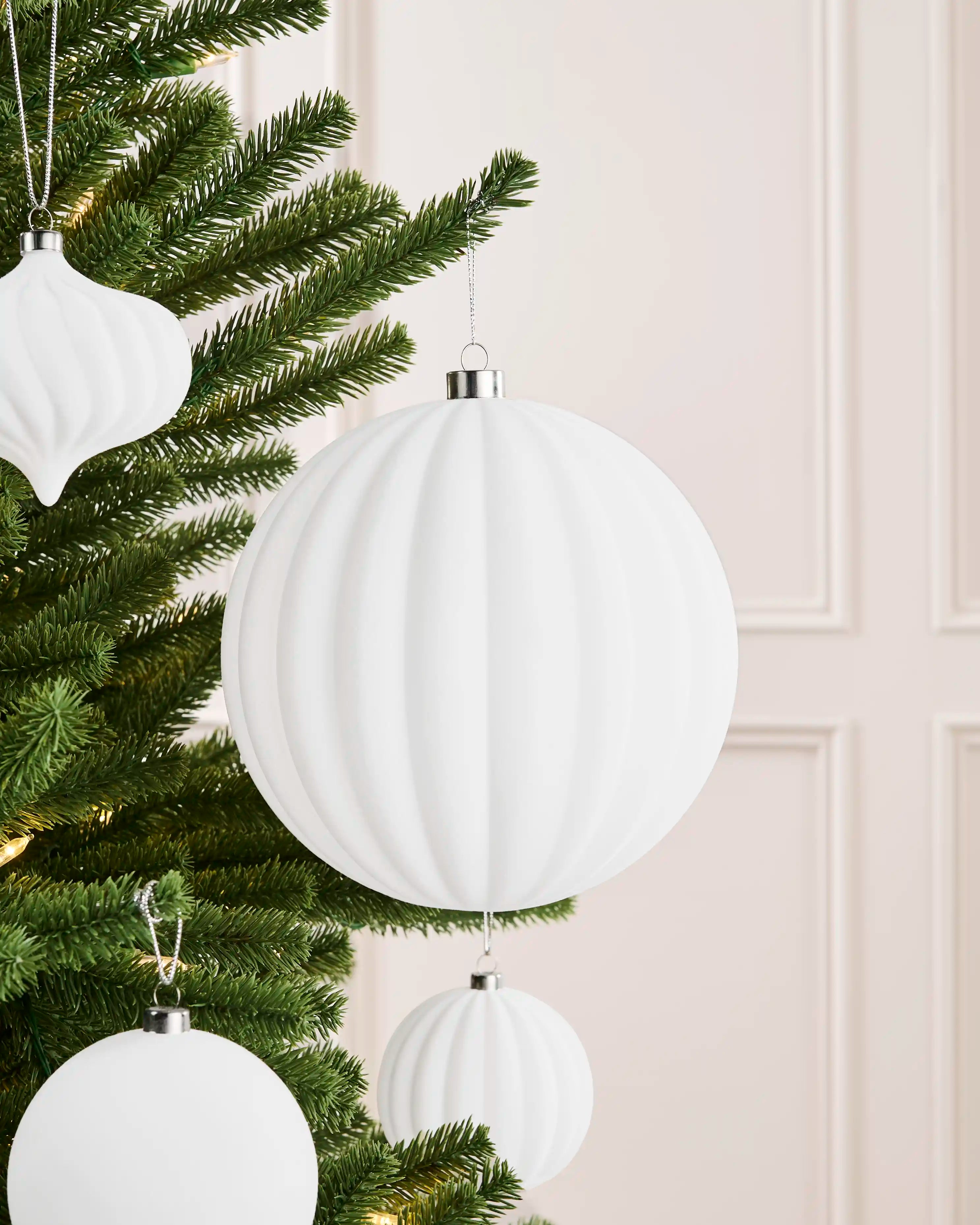 Oversized 20 cm white velvet ribbed bauble styled among matching decorations on a Christmas tree.