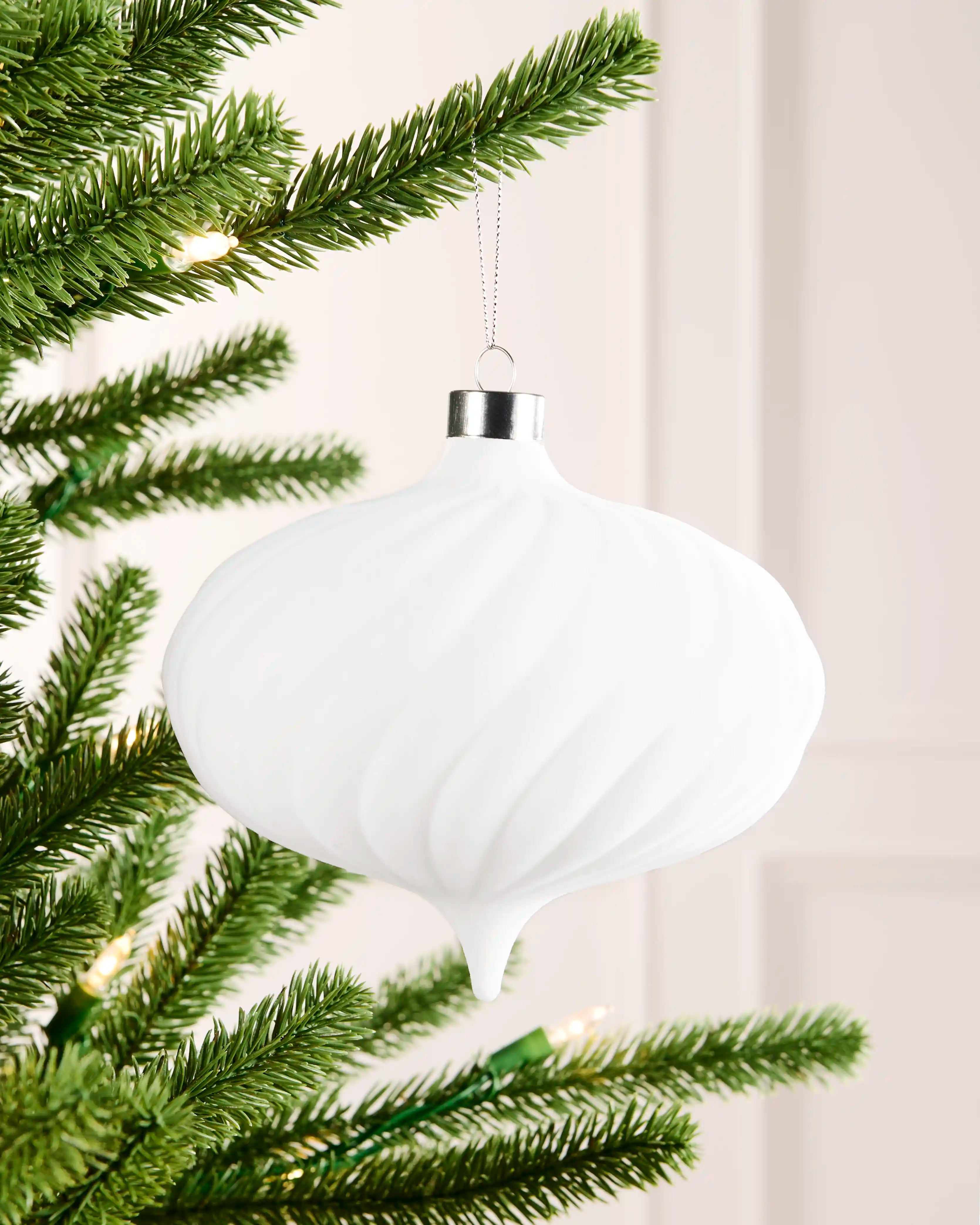 15 cm white oversized velvet spiral ribbed bauble hanging from a Christmas tree with a silver cap and silver hanging string.
