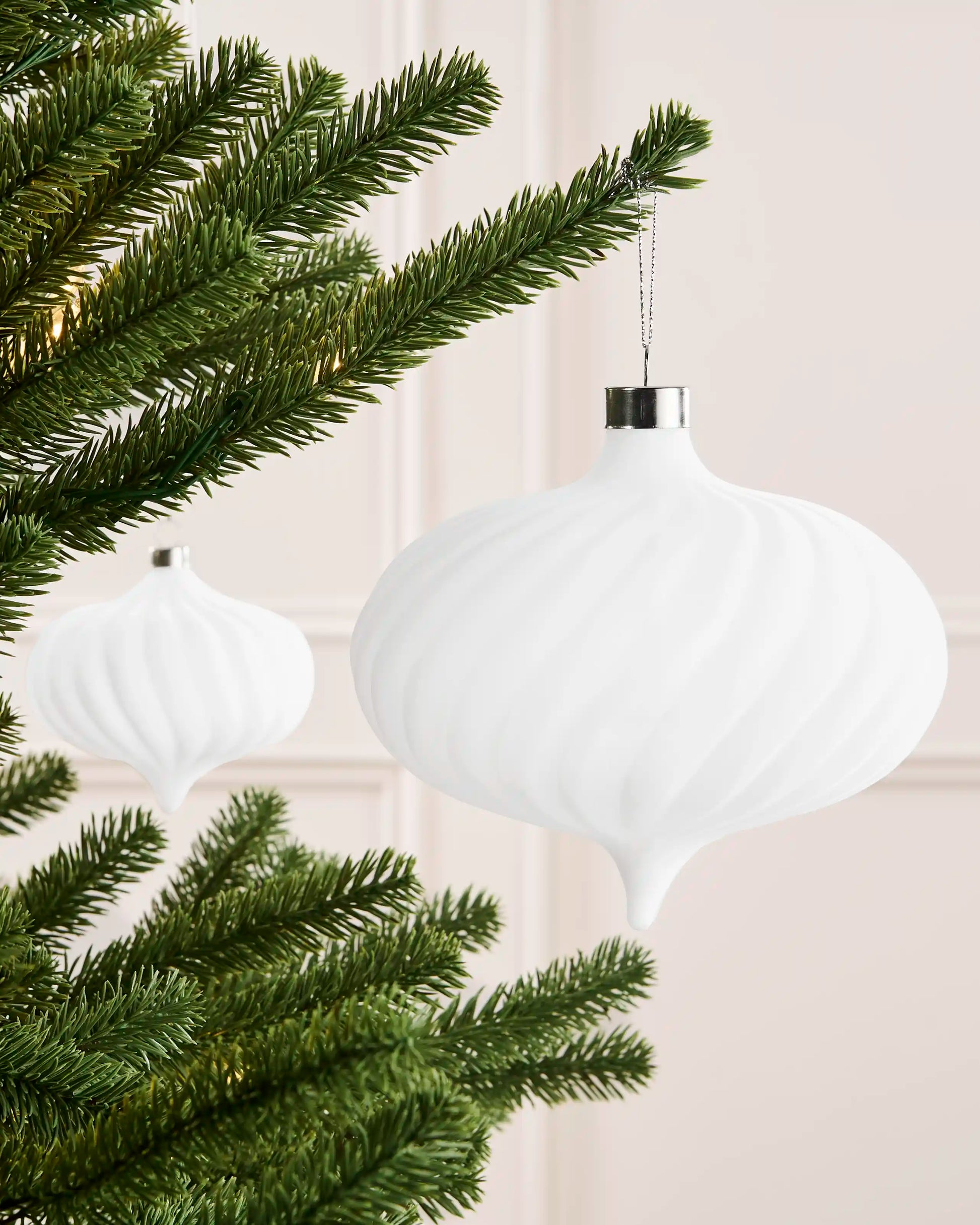 White 15 cm oversized velvet spiral ribbed bauble displayed on a Christmas tree with a matching ornament in the background.