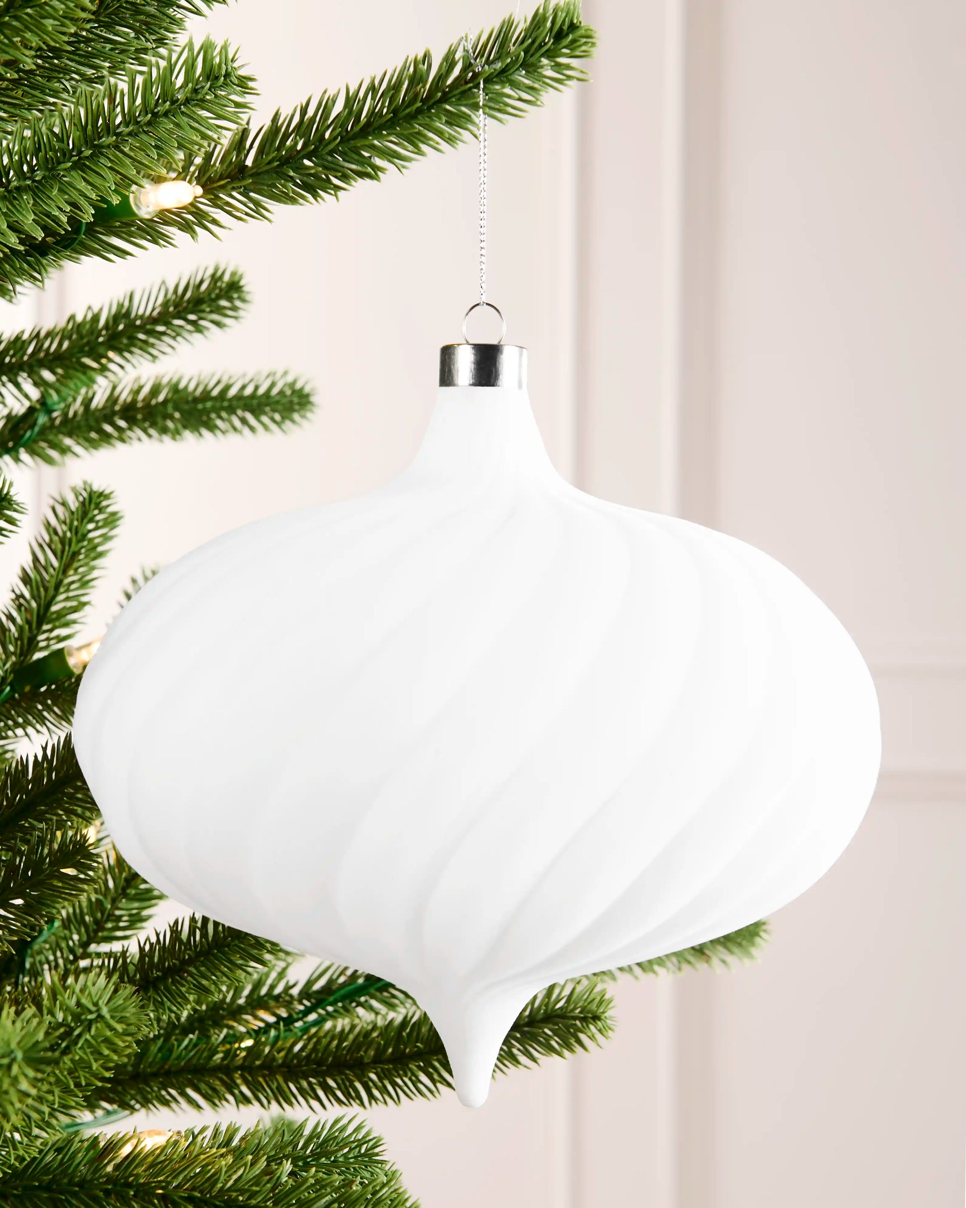 20 cm white oversized velvet spiral ribbed bauble hanging from a Christmas tree with a silver cap and silver hanging string.