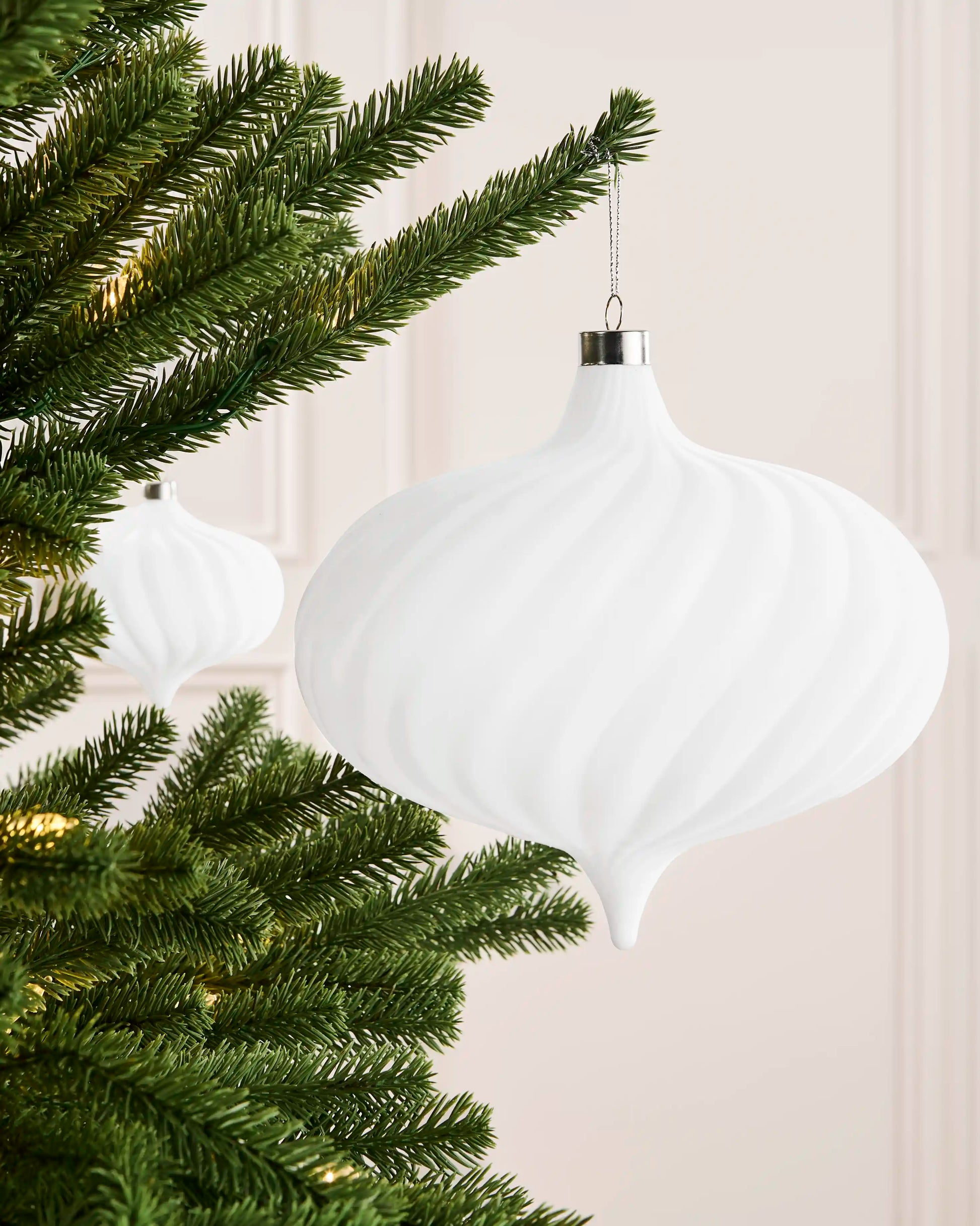 White 20 cm oversized velvet spiral ribbed bauble displayed on a Christmas tree with a matching ornament in the background.