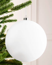 White 20 cm oversized velvet bauble with a traditional round shape, silver cap and hanging string on a Christmas tree.