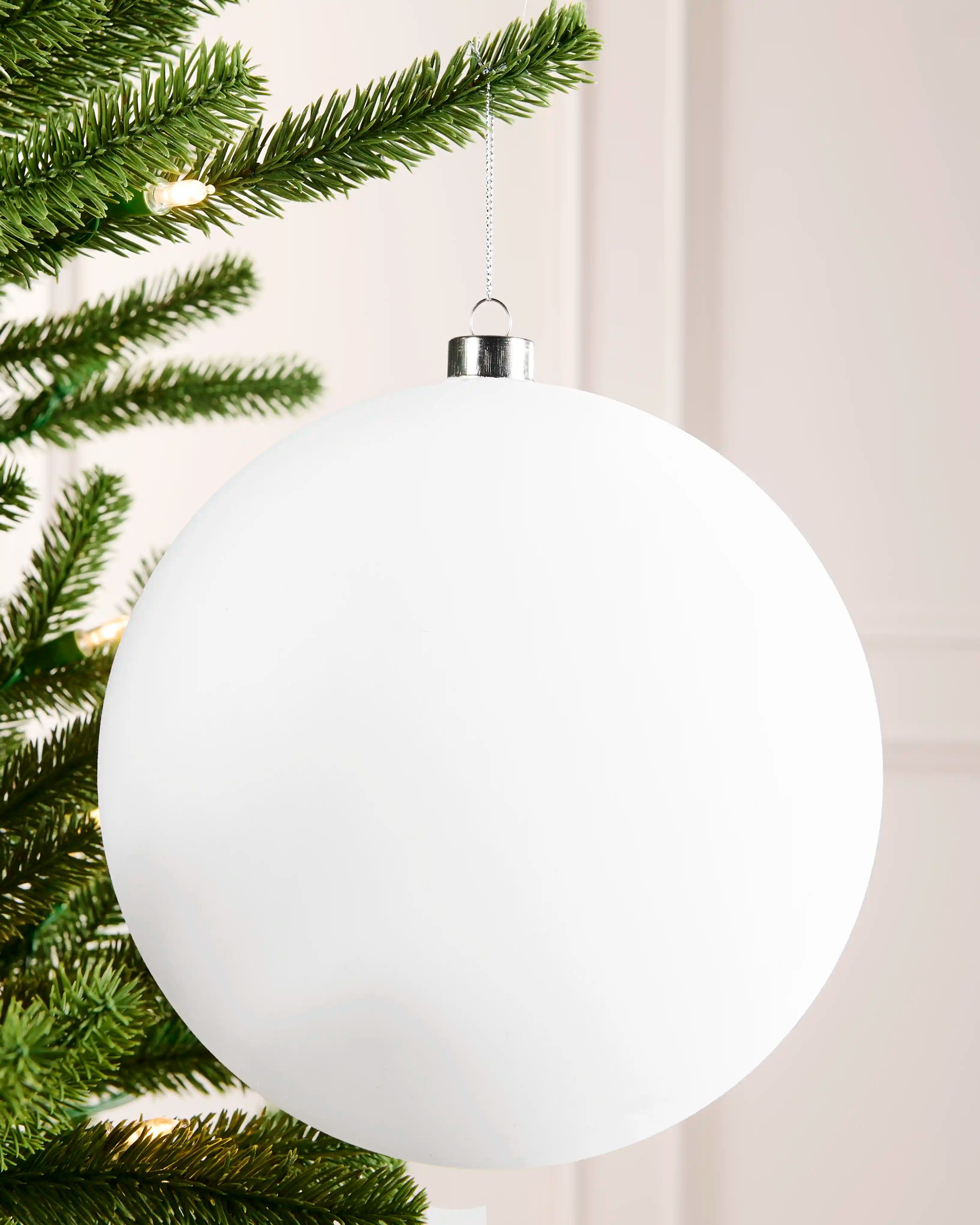 White 20 cm oversized velvet bauble with a traditional round shape, silver cap and hanging string on a Christmas tree.