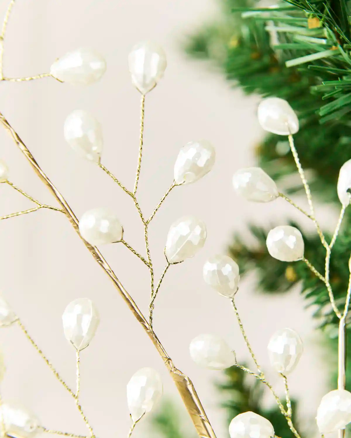 Close-up of white teardrop pearl beads attached to slender gold-toned branches.