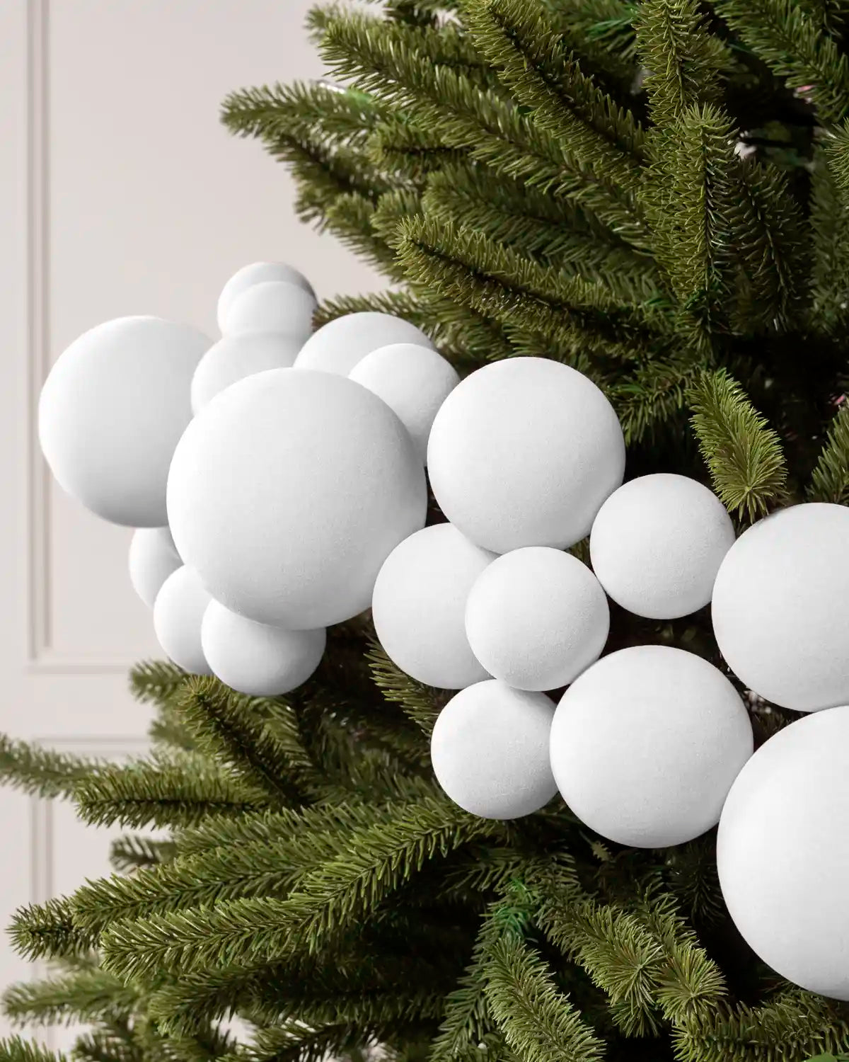 Close-up of white velvet bauble garland on a Christmas tree showing the soft textured finish and mixed bauble sizes.