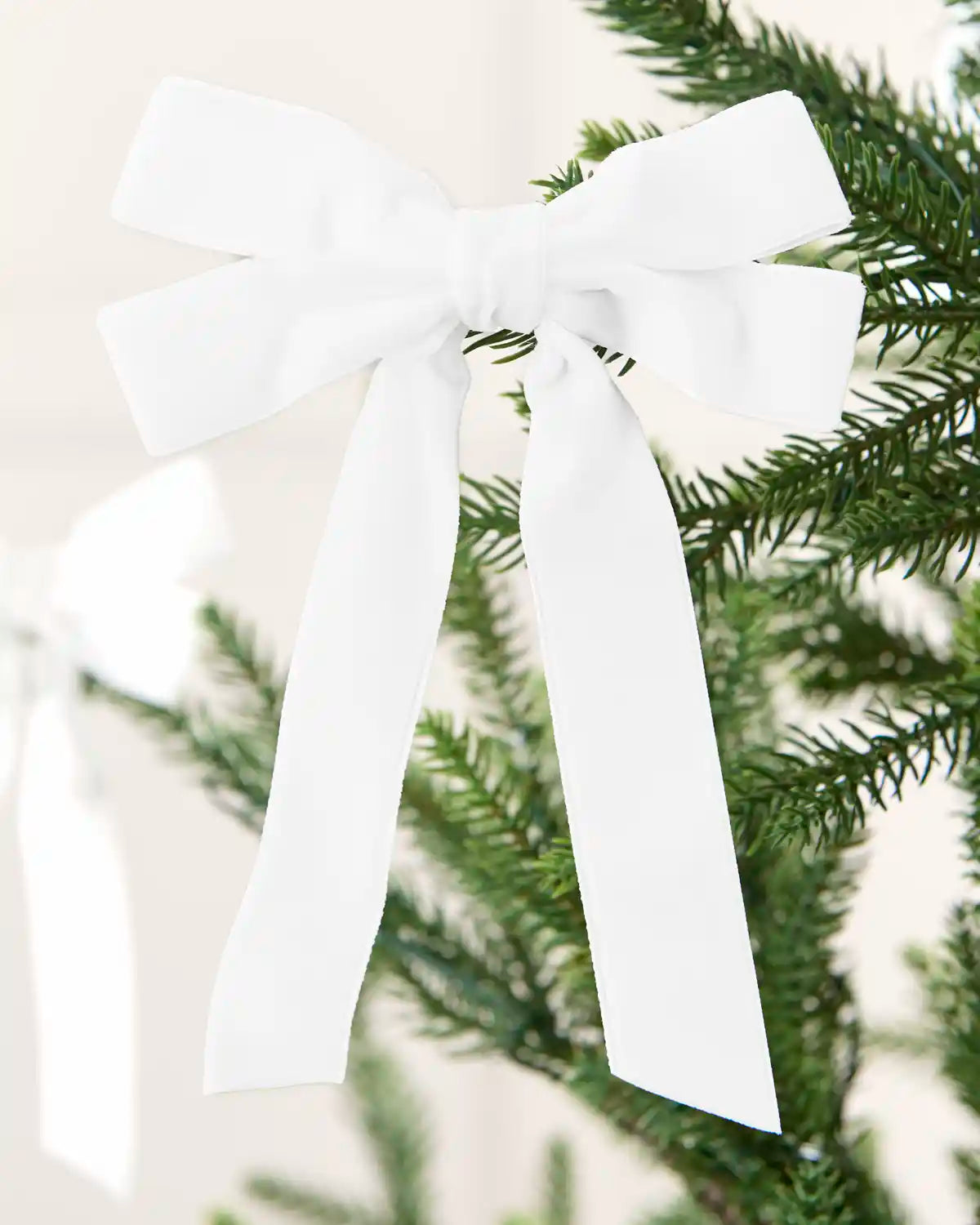 White 16.5 cm velvet double bow with long tails attached to a Christmas tree branch.