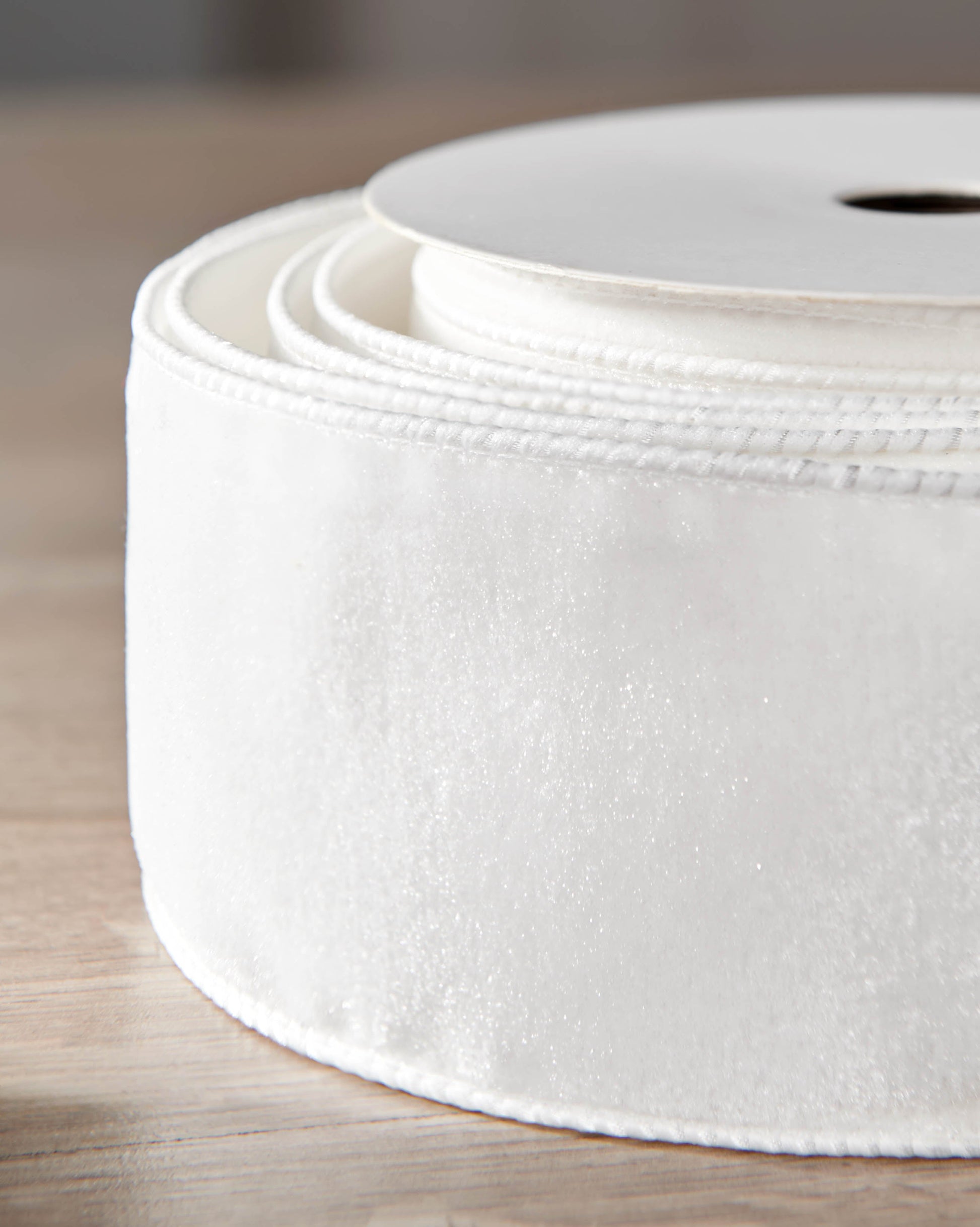 Close-up of white velvet ribbon on a roll, showing the soft texture and wired edge.