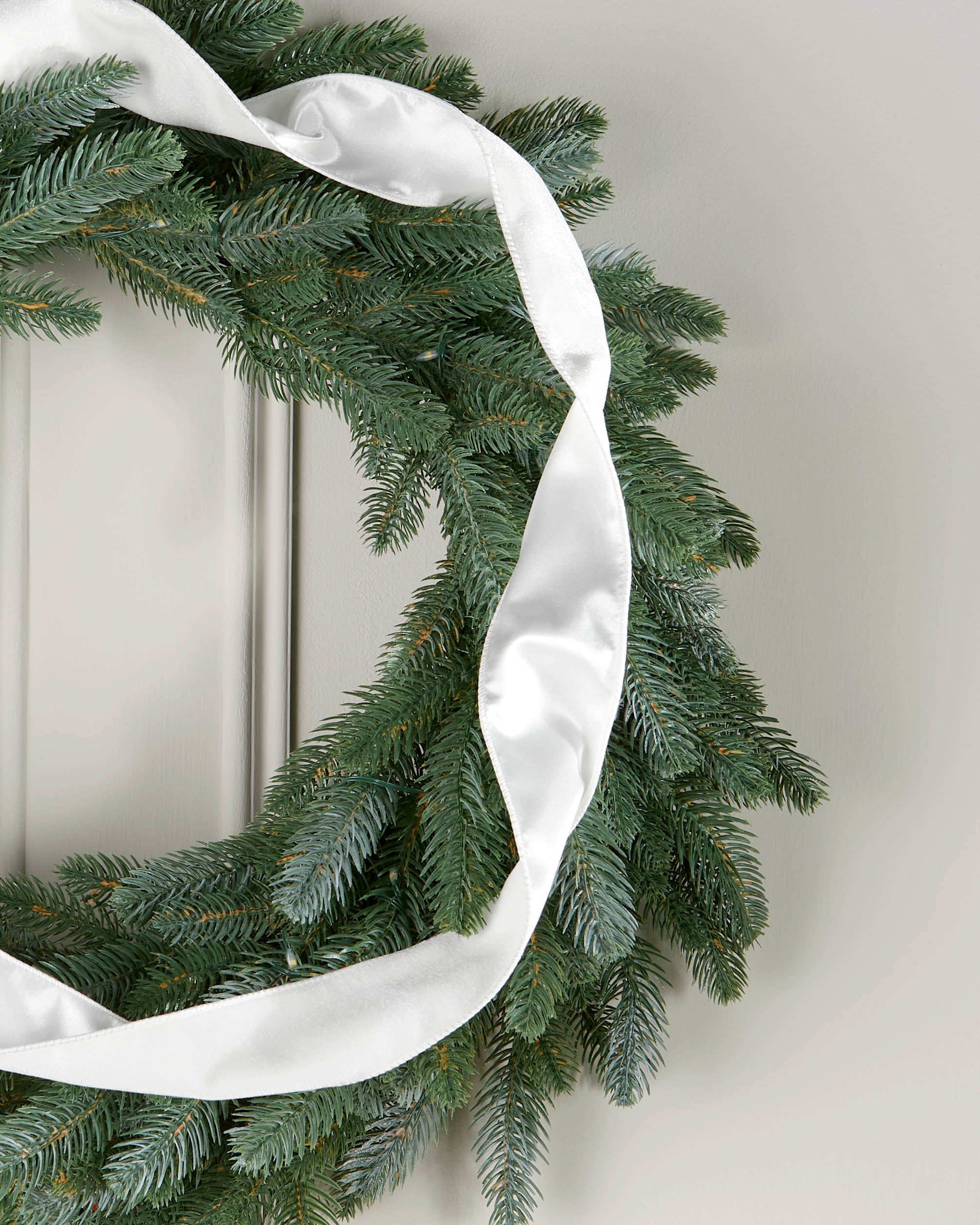 White velvet ribbon styled in a loose spiral on a green Christmas wreath.
