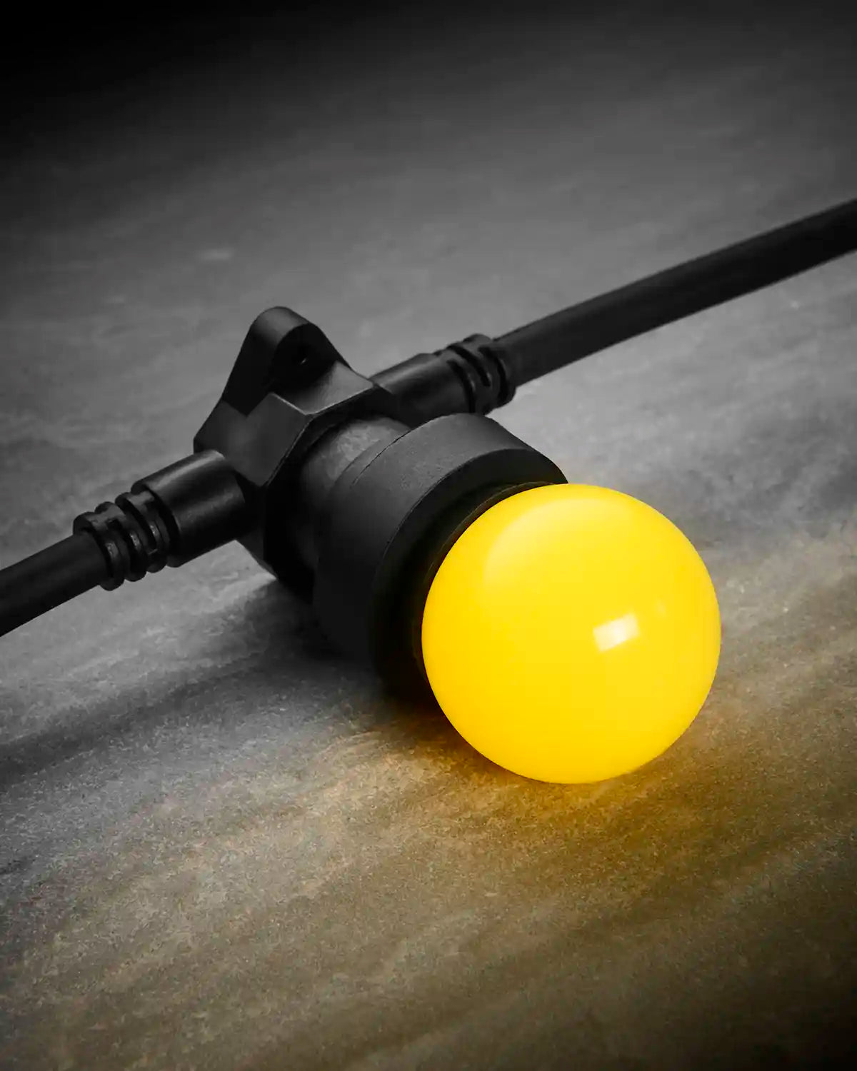Close-up of a yellow E27 LED bulb fitted into a black festoon belt on a dark stone-effect surface.