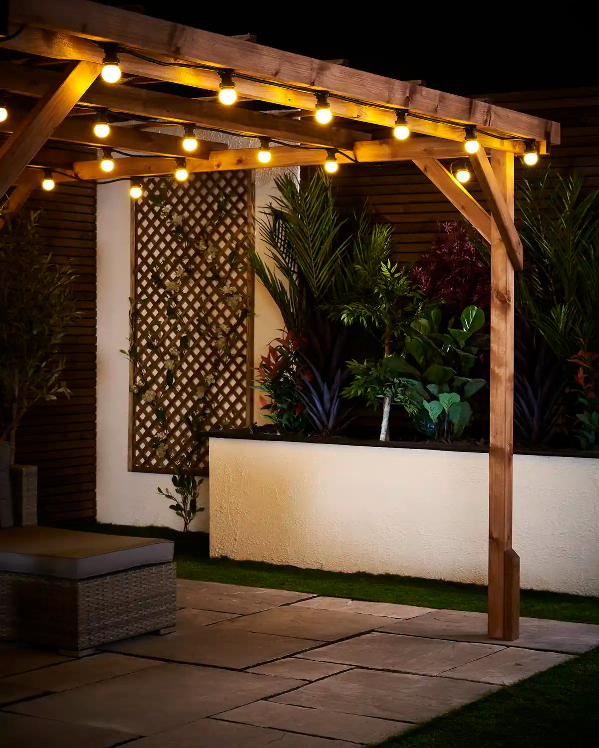Yellow E27 festoon bulbs hanging from a wooden pergola above a paved patio and raised garden bed.