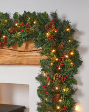 A festive pre-lit extra thick garland with warm white LED lights, pinecones, and red berries displayed on a fireplace mantel.