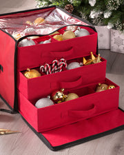 A red, zippered decoration and ornament storage box with multiple compartments, some of which are pulled out, displaying Christmas ornaments inside.