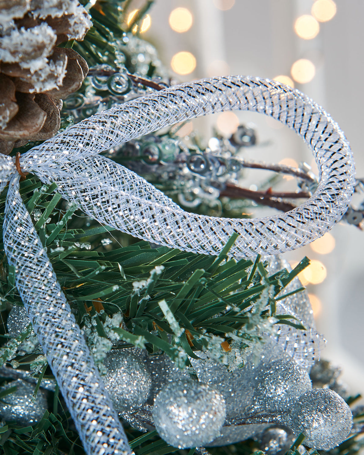 A 2-foot pre-decorated artificial Christmas tree with snow-flocked green branches, red berries, pinecones, baubles, and flowing ribbons, set in a rustic hessian-wrapped base.