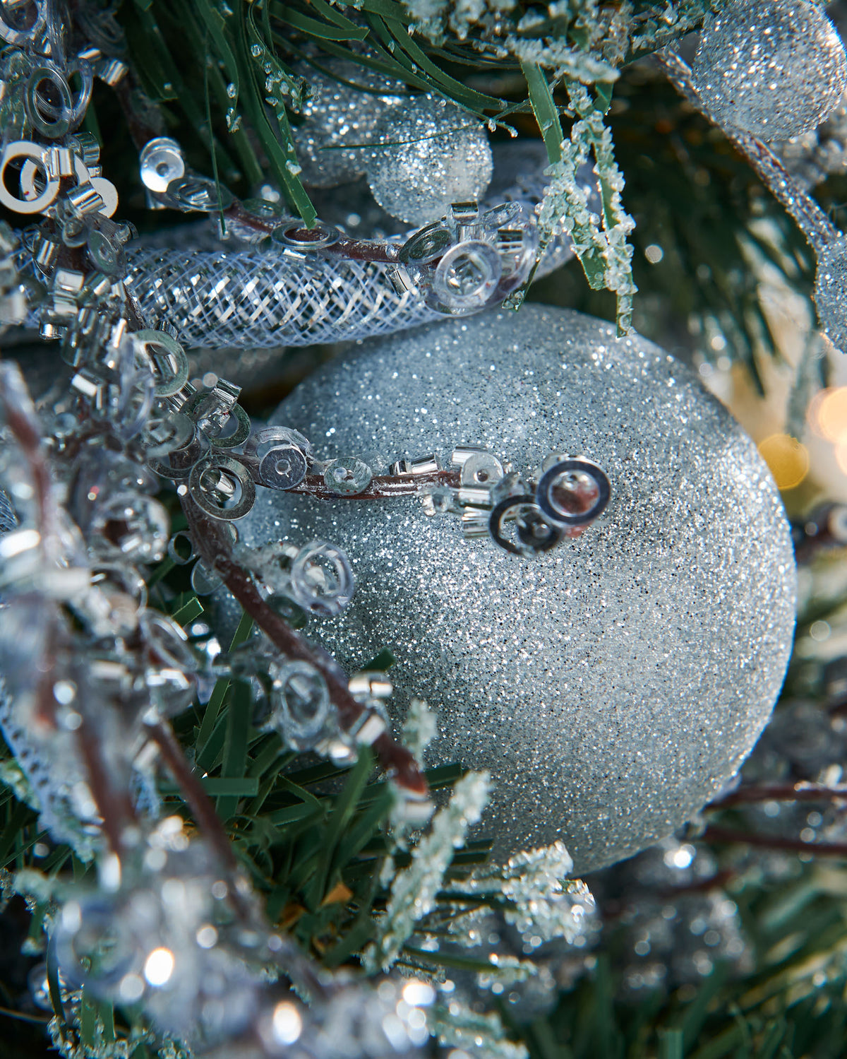 A 2-foot pre-decorated artificial Christmas tree with snow-flocked green branches, red berries, pinecones, baubles, and flowing ribbons, set in a rustic hessian-wrapped base.