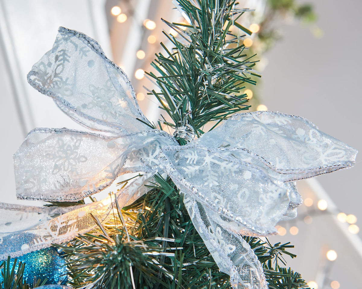 Pre-lit potted decorated Christmas tree with a silver pot, adorned with blue ornaments, white flowers, and green leaves, illuminated with warm white LED lights.