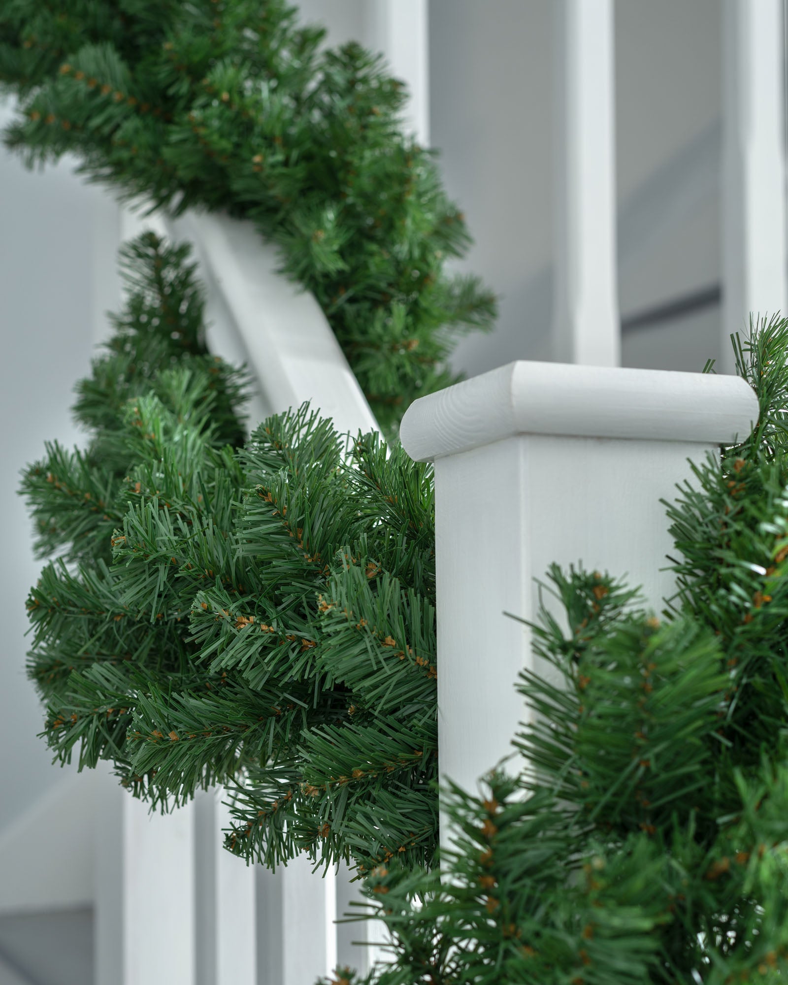 Close-up of plain green pine Christmas garland wrapped around a white staircase banister