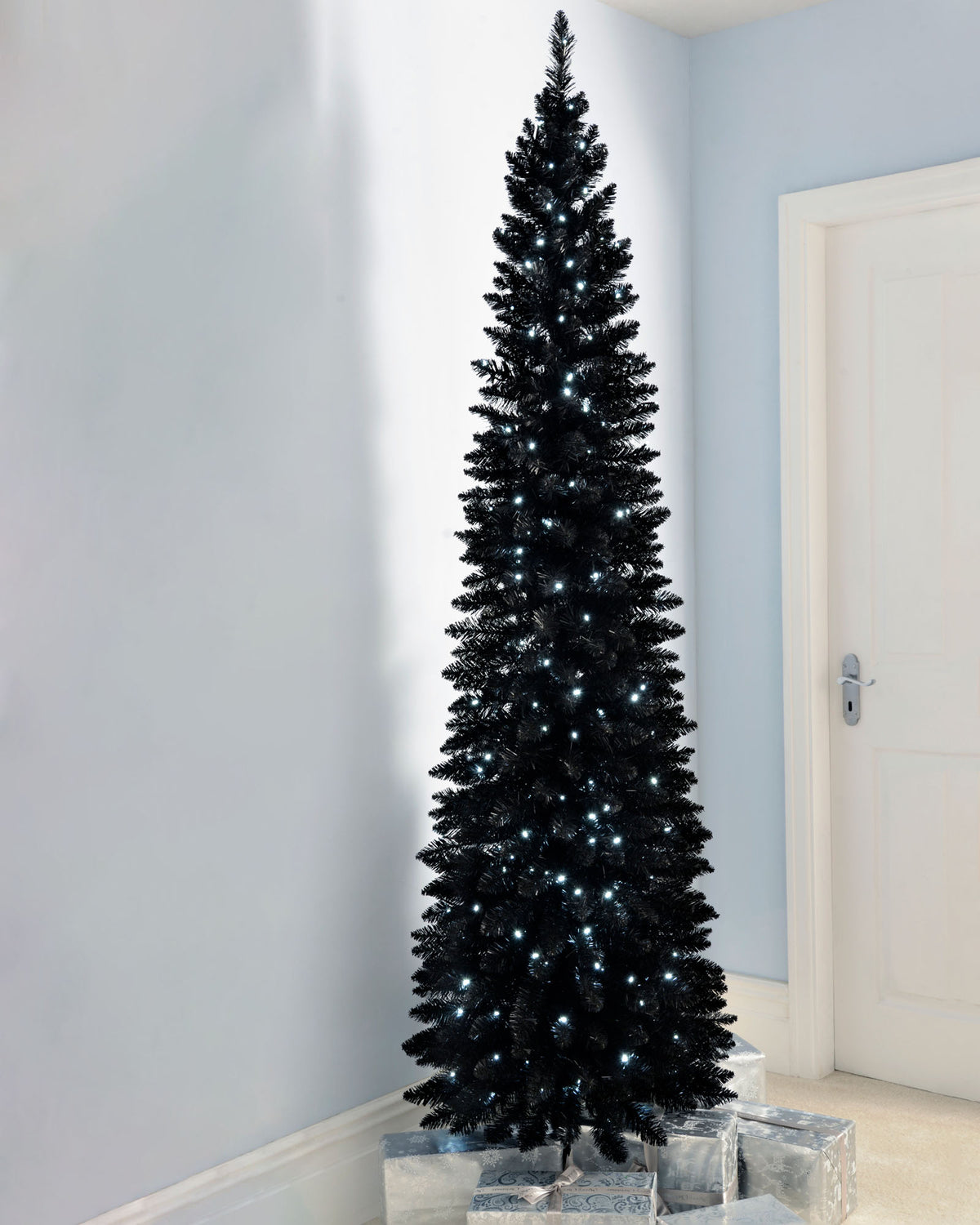 Slim pre-lit black pencil Christmas tree with 400 PE/PVC tips and 180 white LED lights, placed in a room corner—modern and elegant with a radiant glow, ideal for compact or stylish festive spaces.