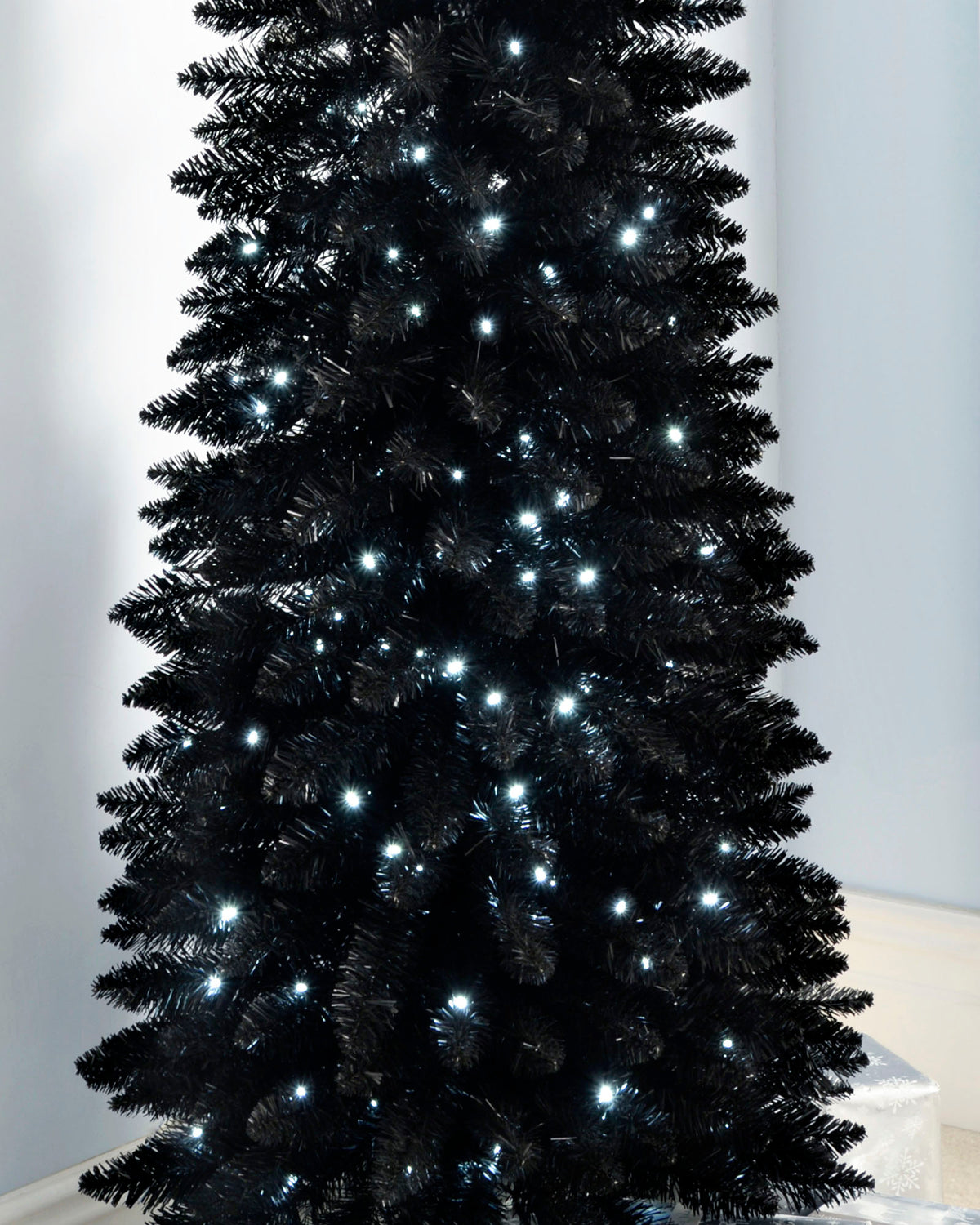 Slim pre-lit black pencil Christmas tree with 400 PE/PVC tips and 180 white LED lights, placed in a room corner—modern and elegant with a radiant glow, ideal for compact or stylish festive spaces.