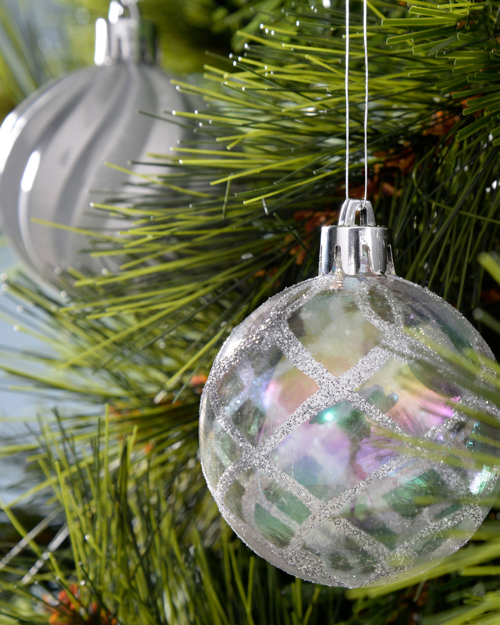 Iridescent silver 6cm shatterproof bauble hanging on a green Christmas tree